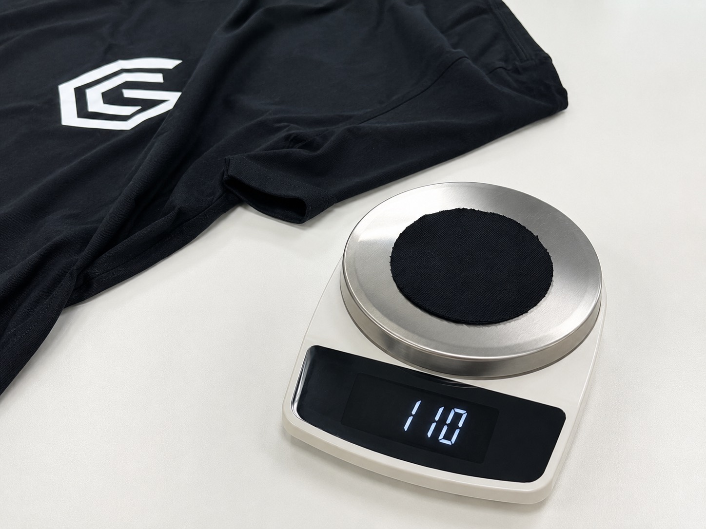 A swatch cut from the original shirt on a laboratory scale reading 110, next to the black shirt
